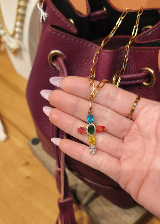 Collier doré avec croix strass multicolores, pièce colorée portée sur une main en boutique