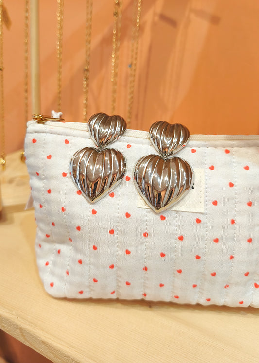 Boucles d’oreilles pendantes double cœurs striés argenté, posées sur trousse blanche avec petits cœurs rouges en boutique