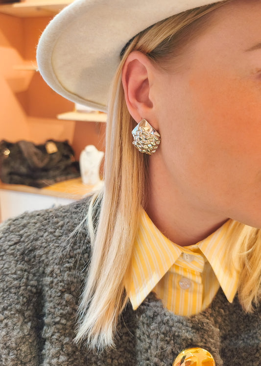 Boucles d’oreilles superposition de carrés argentés portées avec un chapeau, look stylé en boutique
